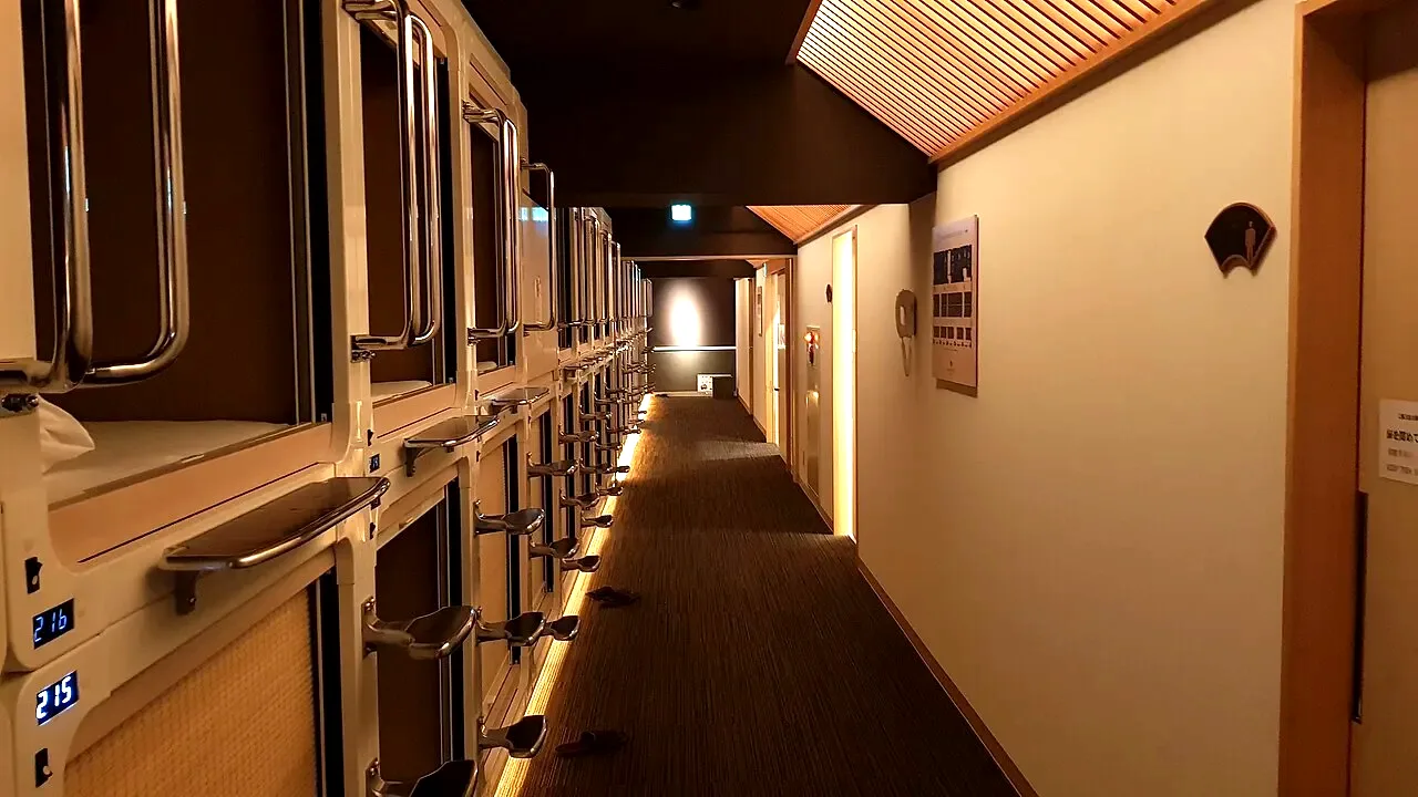 A warm, wood-panelled corridor of capsule pods in a Japanese capsule hotel